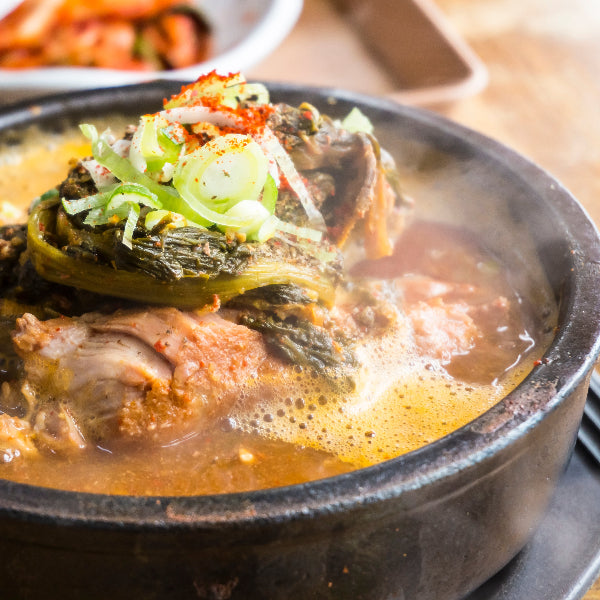 Hot pot dish with vegetables and broth in a black pot on a wooden table.