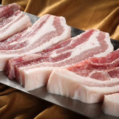 Raw pork belly slices on a metal tray with a brown fabric background